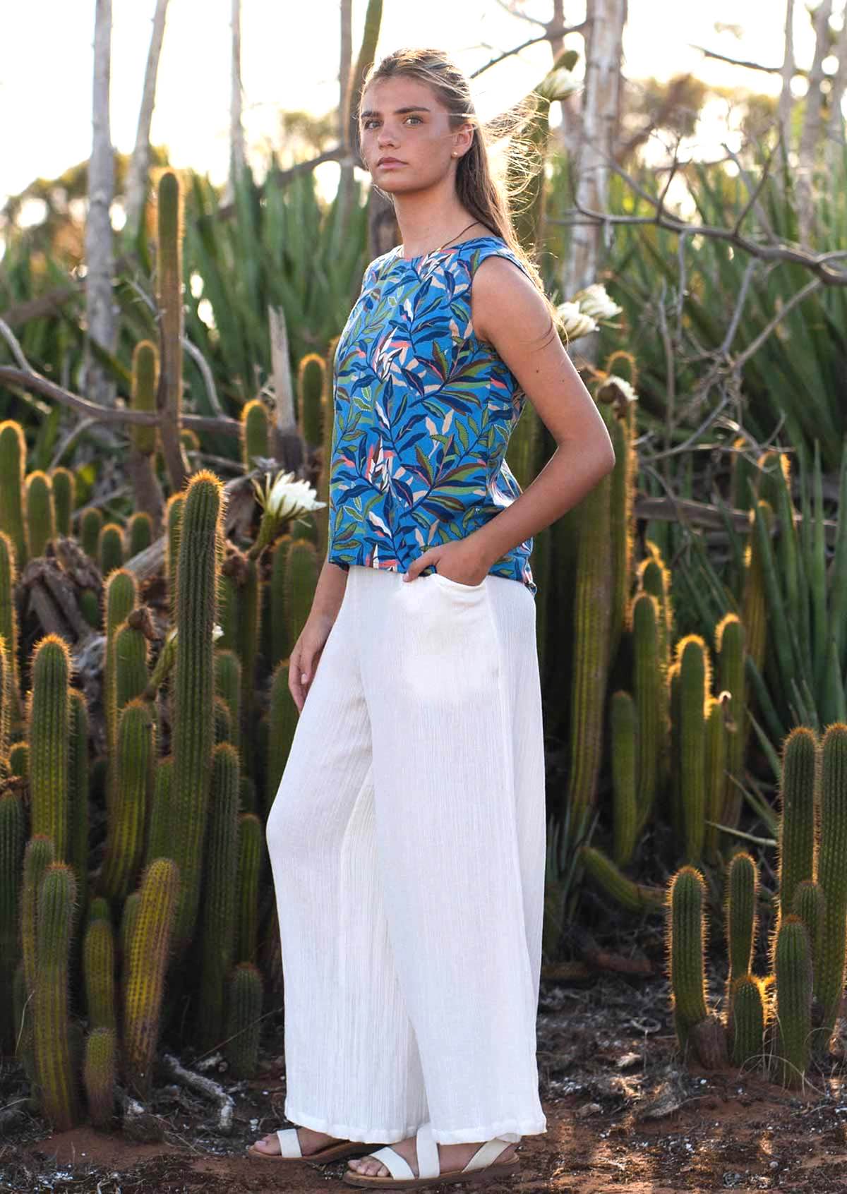 woman wearing wide legged white cotton pants and blue cotton top with hand in pocket
