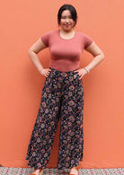 Model standing against wall with hands on hips wearing black and floral print 100 percent rayon womens palazzo pants