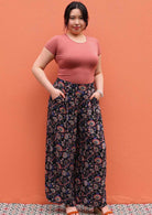 Model standing against wall with hands in pocket wearing black and floral print 100 percent rayon womens palazzo pants