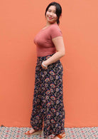 Model standing side on with hands in pocket wearing black and floral print 100 percent rayon womens palazzo pants