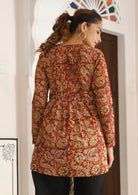 Woman wears cotton long sleeve top in floral print with warm toned rusty base, that is longer at the back 
