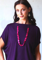 Woman wearing fuchsia pink wood bead necklace over purple t-shirt
