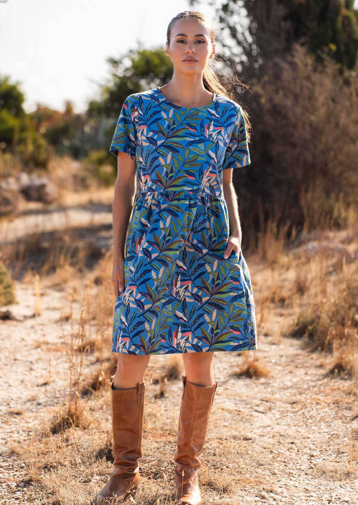 Woman wearing 100 percent cotton blue base retro dress with leafy print with one hand in pocket