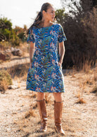 Woman wearing 100 percent cotton blue base retro dress with leafy print with hands in pockets