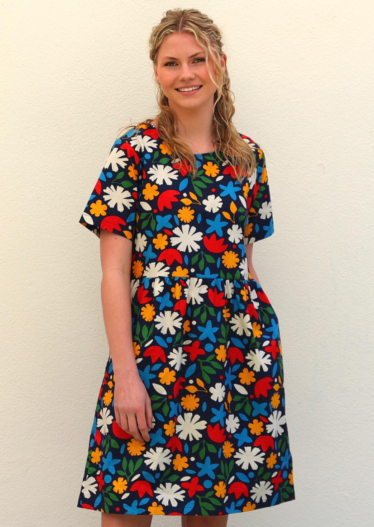 Model with blonde hair  wearing 100 percent cotton dark navy blue base and bright abstract floral retro print cotton dress