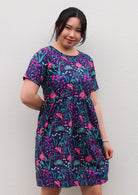 woman in loose fit purple, navy and pink floral print 100% cotton dress in front of hands behind back 