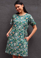 Model with dark hair in loose fit green cotton floral dress with hands in pockets 