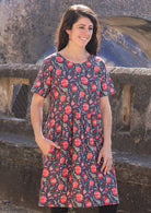 Woman looking to the side wearing 100 percent cotton blue base retro dress with leaf and floral print with one hand in pocket