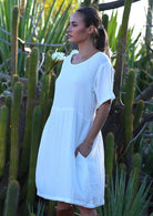 Woman with dark hair wearing natural white double cotton short sleeve relaxed fit dress with side pockets