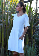 Woman with dark hair wearing natural white double cotton short sleeve relaxed fit dress with side pockets