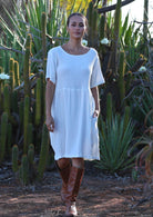 Woman with dark hair wearing natural white double cotton short sleeve sundress in front of cacti
