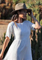 woman wearing white 100%  cotton maxi dress with hat in front of cacti 