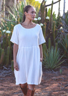 Woman with dark hair wearing white pure 
cotton short sleeve sundress in front of cacti 