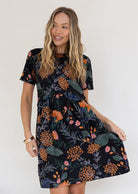 Woman poses in loose fitting gorgeous black based cotton dress with blue, grey and green leafs and orange, pink florals.