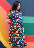 Woman stands in cotton short sleeve midi length dress in fun bold floral print on a dark blue base