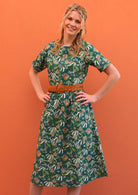 Model with hands on hips wearing 100 percent green cotton sundress with sleeves and waist belt