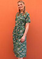 Model standing with one hand in pocket wearing 100 percent green cotton sundress with sleeves 