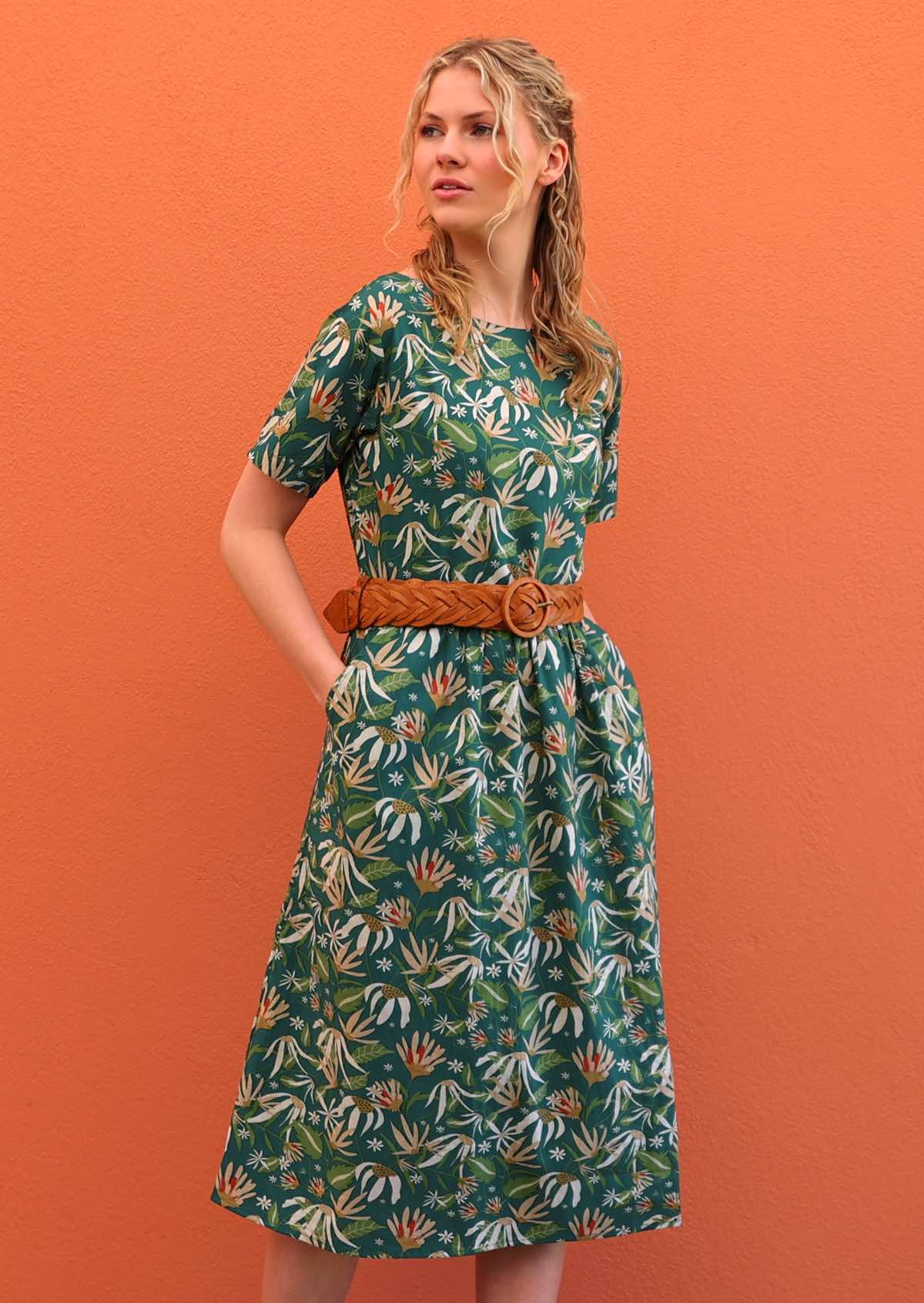 Model with hands in pockets wearing 100 percent green cotton sundress with sleeves and waist belt