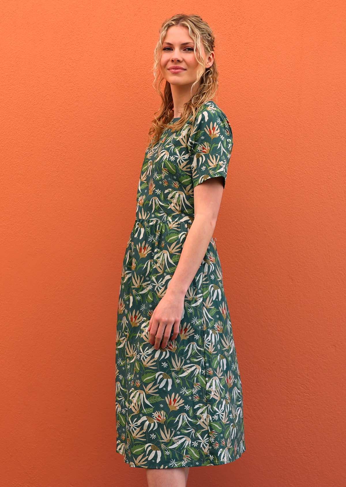 Model standing side on wearing 100 percent green cotton sundress with sleeves 