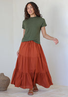 Woman wearing a green top and rust shade skirt with elasticated waistband standing against a white background