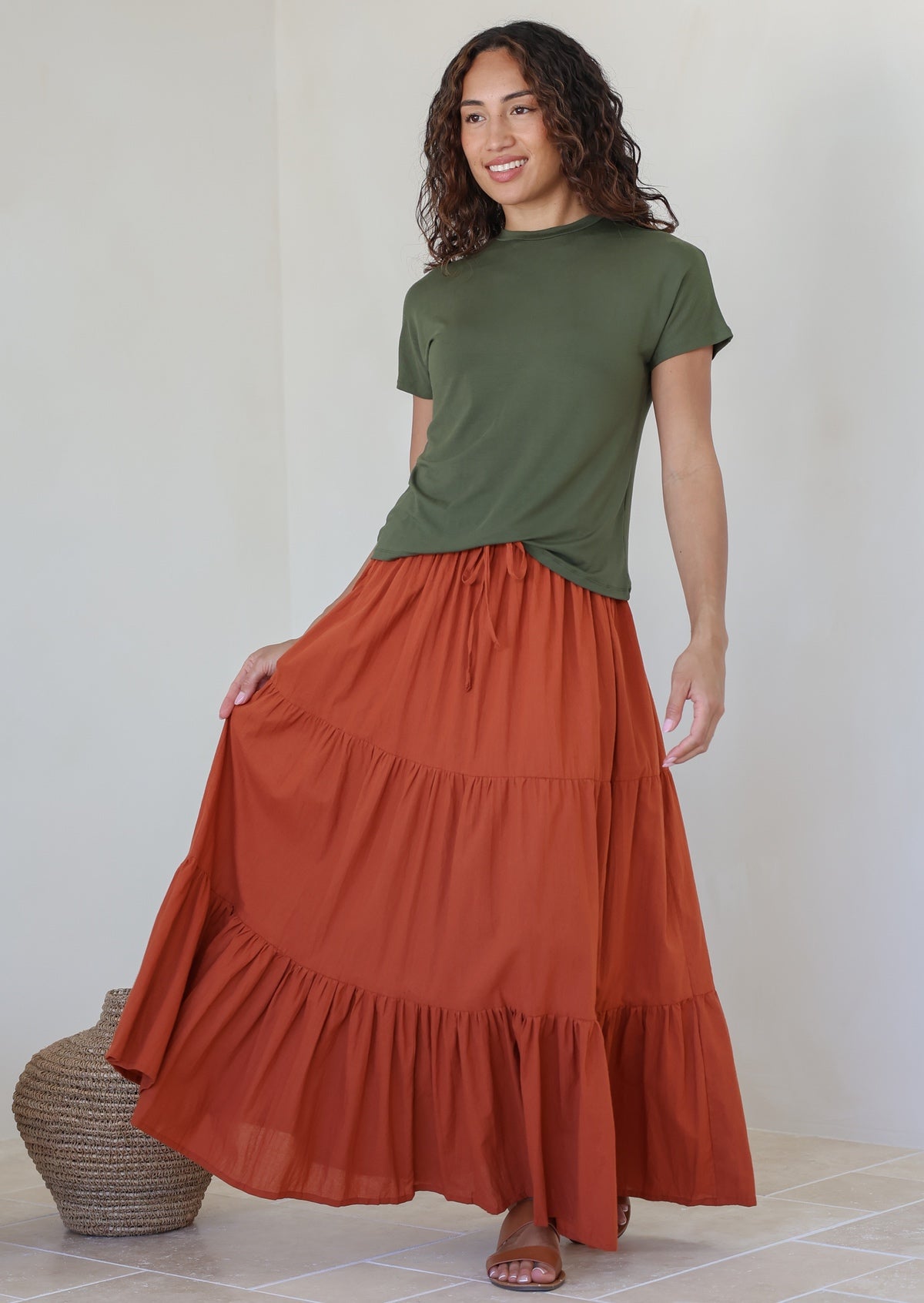 women wearing a 100% cotton rust shade skirt with a green plain top standing against a white background.