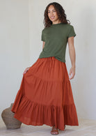 women wearing a 100% cotton rust shade skirt with a green plain top standing against a white background.