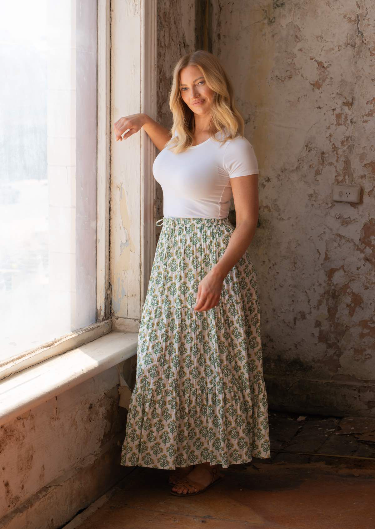 woman standing in front of old warehouse window in white cotton maxi skirt with yellow flowers