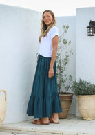 Woman wearing a white top and deep teal cotton skirt with elasticated waistband standing outdoors