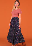 Model standing side on wearing dark Purple 100 percent cotton Indian floral printed three tiered maxi skirt 