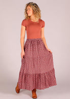 Model standing holding top tier of  100 percent cotton three tiered maxi skirt in dark terracotta  