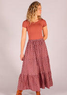 Model standing wearing 100 percent cotton three tiered maxi skirt in dark terracotta  