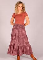 Model standing with hands behind back wearing 100 percent cotton three tiered maxi skirt in dark terracotta  