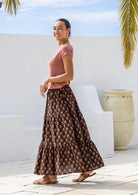 Side pose of model wearing tiered cotton maxi skirt with floral motifs and elasticated waist.
