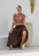 Woman wearing 100%^ cotton flowy maxi skirt in brown based floral print with elasticated waist and drawstring.