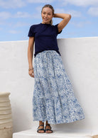 Woman wearing a white based blue floral cotton skirt standing against a white wall.