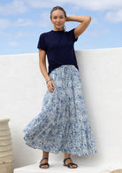 Woman wearing a white based blue floral cotton skirt standing against a white wall.