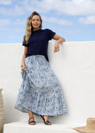Woman wearing a white based blue floral cotton skirt standing against a white wall.