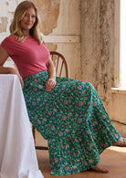 Model sitting in wooden chair wearing three tiered 100 percent cotton maxi skirt with elasticated waistband and drawstring