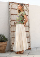 Woman wearing a green floral top and white plain cotton skirt with elasticated waistband standing outdoors