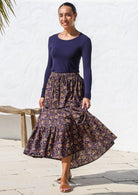 Model posing in a flowy cotton maxi skirt in dark purple based floral print, paired with long sleeve stretch top in navy blue.