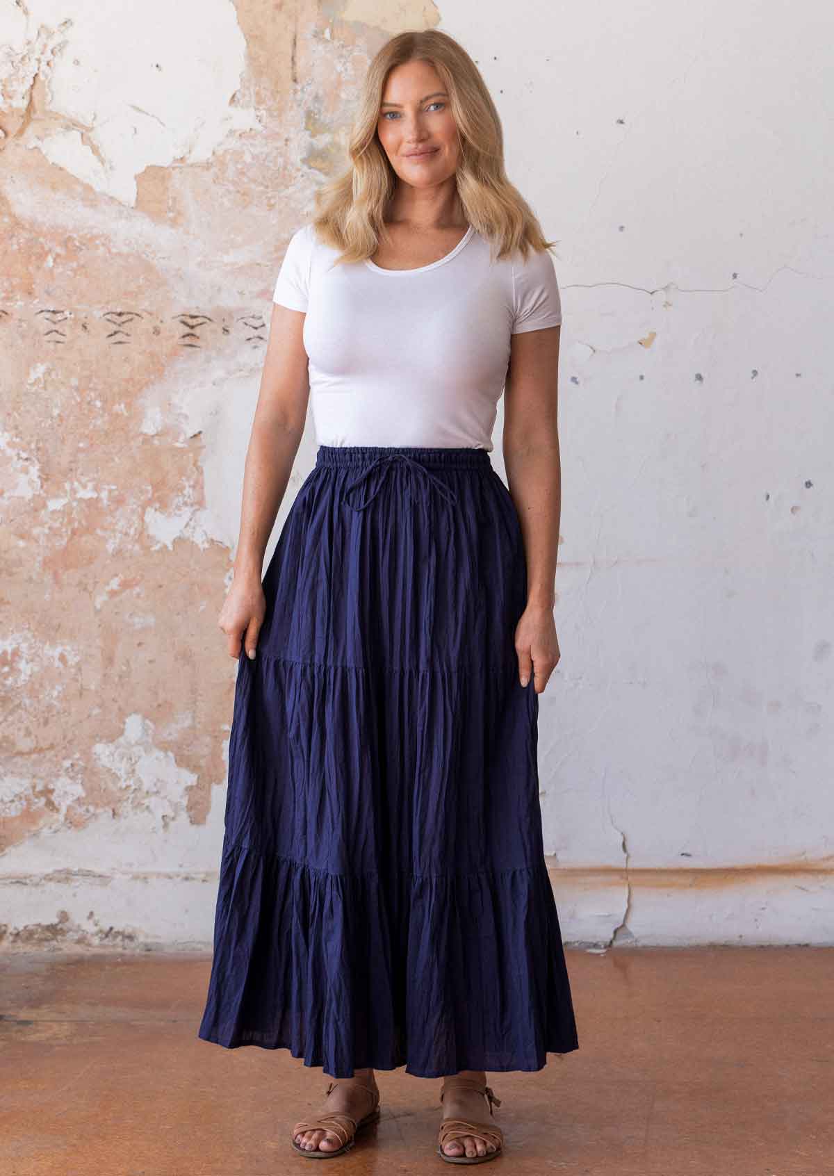 Woman stands in cotton three tiered maxi skirt in dark vibrant blue paired with white stretch rayon t-shirt