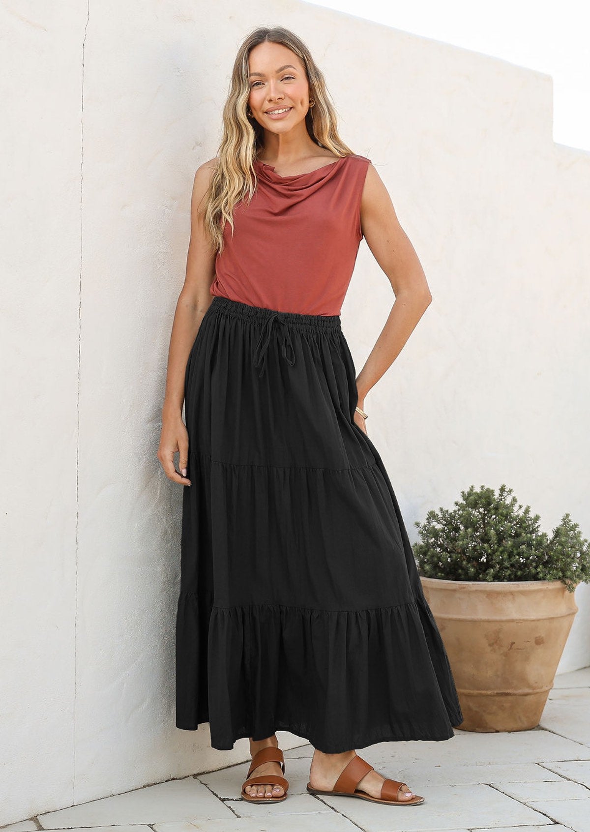 Woman wearing a black cotton maxi tiered maxi skirt with a pink sleeveless toop and tan sandals