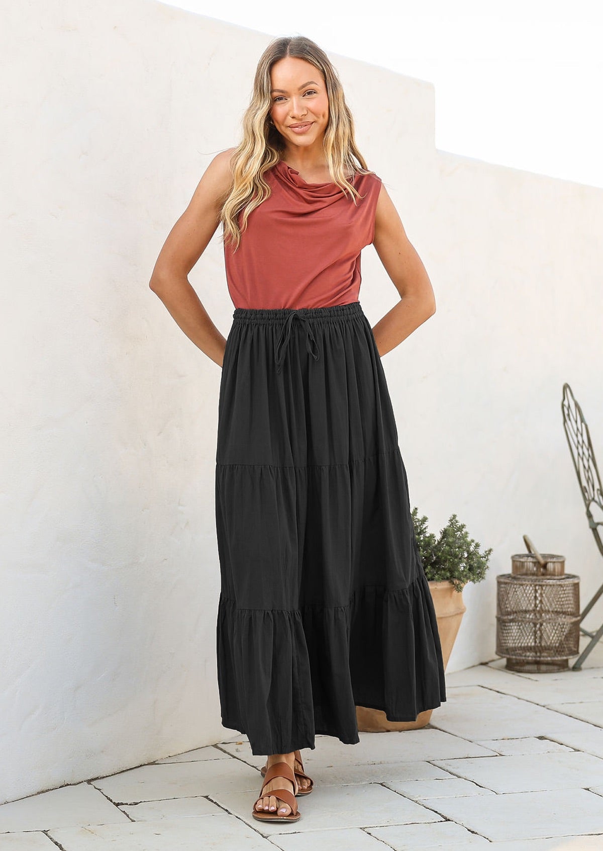 Woman wearing a pink sleeveless top and black cotton tiered maxi skirt with shoestring waist tie