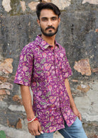 Man wears short sleeve cotton button through shirt in purple based floral print