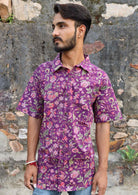 Man wears cotton relaxed fit shirt with collar, one pocket and coconut buttons, in purple based floral print