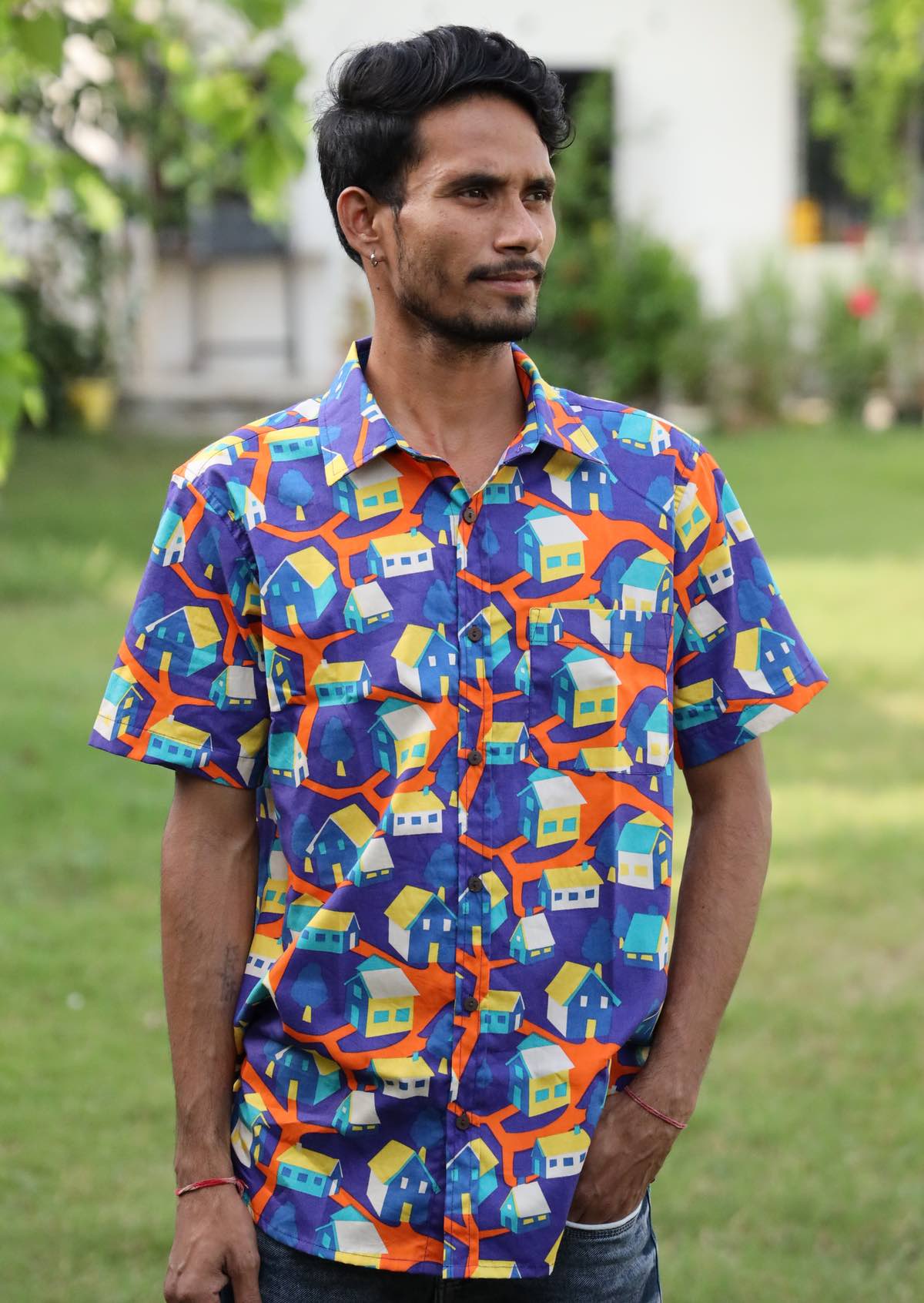 Man wears bright cotton shirt in fun retro house print in orange, yellow, aqua and blue