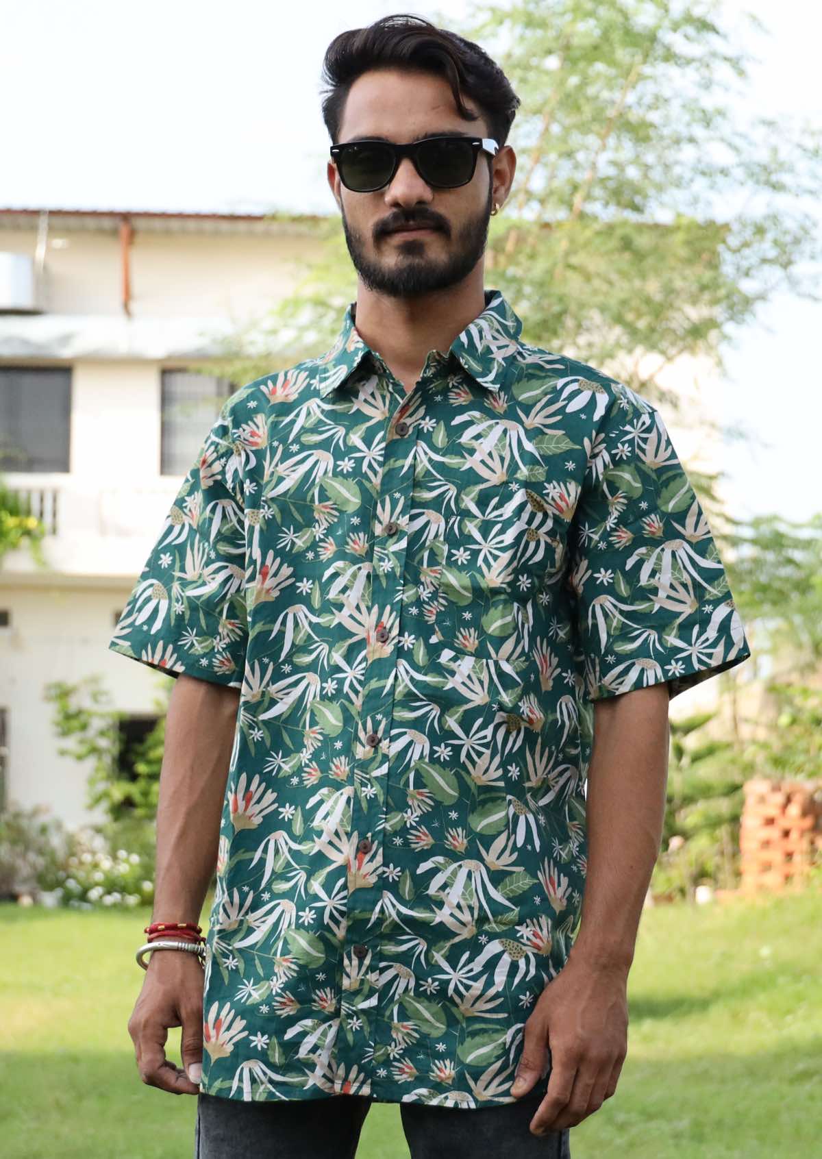 Man wears cotton button through shirt with earthy toned floral on a dark green base