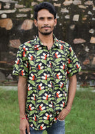 Man poses in cotton relaxed fit short sleeve shirt in striking green, orange and white botanical print on a black base