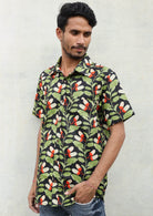 Man leans on wall in cotton relaxed fit button through shirt in graphic botanical print with black base