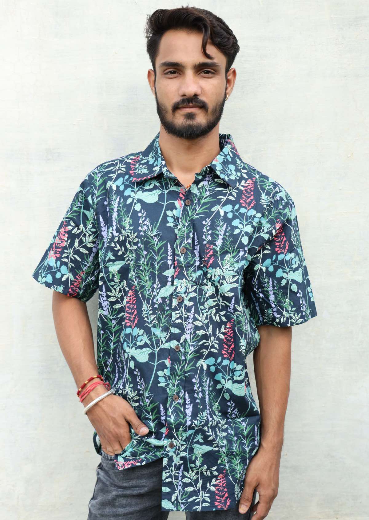 Man poses in teal based floral print cotton short sleeved shirt with collar and coconut buttons